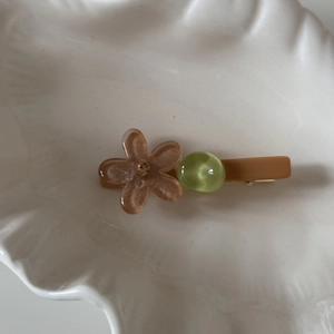Detalle de la pinza para el pelo con flor de color caramelo, purpurina y cuenta verde