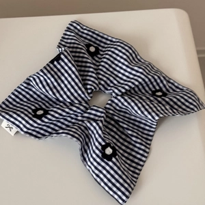 Detailed macro view of blue and white checkered scrunchie with black floral embroidery