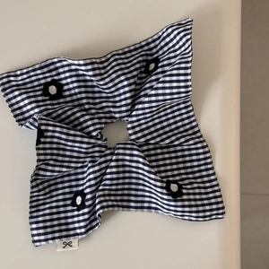 Detail of blue gingham scrunchie with floral embroidery and a small bow label