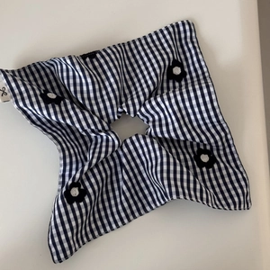 Detail of blue gingham scrunchie with knit flower charms and woven label on white background