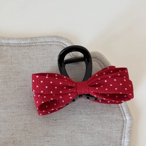 Vue détaillée d'une pince à cheveux à nœud rouge à pois sur un support en lin gris