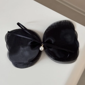 Détail d'un nœud en résille noire multicouche avec pendentif perle blanche sur fond blanc