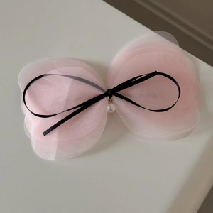 Détail d'une pince à cheveux en tulle rose avec ruban noir et pendentif perle