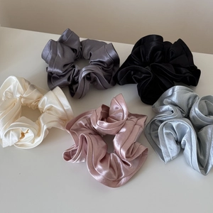 Close-up of five pearlescent satin scrunchies in grey, black, cream, pink, and blue tones