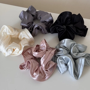 Flat lay macro detail of five satin silk scrunchies in assorted elegant neutral colors