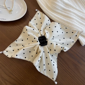 Détail d'un nœud à cheveux en mousseline beige avec cœurs noirs et perles sur bois