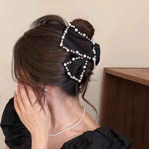 Detail of elegant black satin bow hair claw with white pearls shown on a woman hairstyle