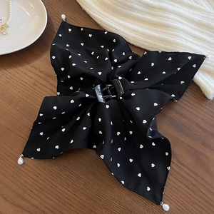 Détail d'un nœud à cheveux noir avec motif cœur et perles blanches sur fond de bois sombre