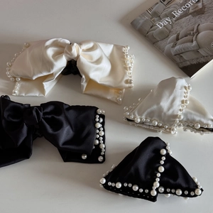 Detail view of satin bow hair clips with pearl trim in elegant black and off-white colors