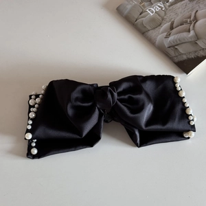 Close-up of black satin bow hair claw clip with delicate pearl trim on white background