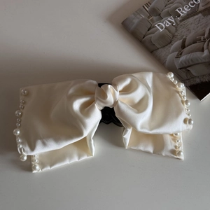 Detail shot of a beige satin bow hair claw clip with delicate pearl trim on smooth surface