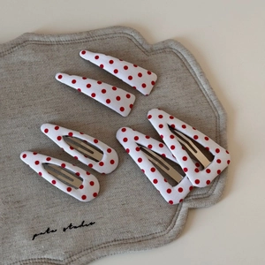 Detail showing set of six white and red polka dot hair clips on soft linen fabric