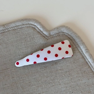 Close-up of white fabric snap clip with red polka dots on textured linen background