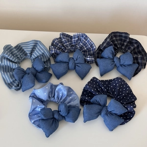 Detail view of five denim blue bow scrunchies featuring stripes, checks, and star patterns
