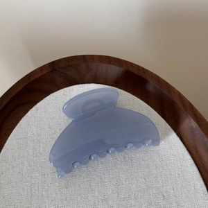 Détail d'une pince à cheveux bleu clair translucide sur un plateau en bois épuré
