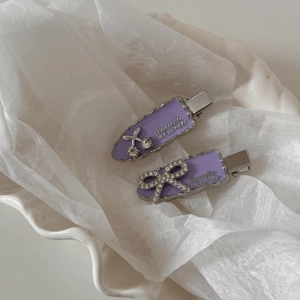 Détail de barrettes violettes avec cerise en strass et nœud sur un bol en céramique blanc