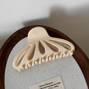 Detail view of a cream fan-shaped cutout hair claw on a decorative wooden tray