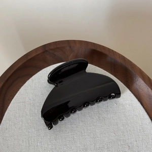 Gros plan sur la pince à cheveux noire brillante en forme d'éventail sur lin beige