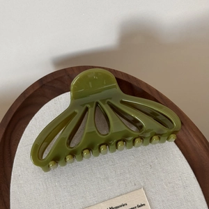 Detail view of glossy olive green hollow fan-shaped hair claw clip on linen