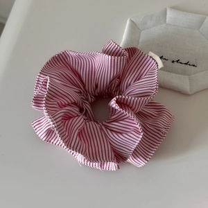 Détail d'un chouchou en tissu à rayures rouges et blanches avec texture plissée et décor épuré