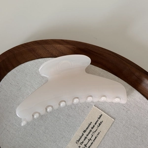Detail of large cream white arc hair claw clip on a minimalist linen display tray