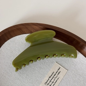 Detailed macro view of olive green glossy curved hair claw clip on wooden tray