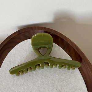 Detail view of a glossy dark olive green hair claw clip on elegant linen background