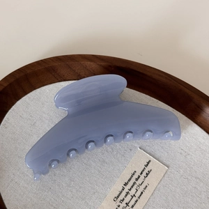 Top view of a translucent light blue oversized hair claw clip on a wooden tray