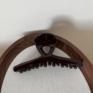 Close-up of a glossy deep red hair claw clip on a circular wooden tray with shadows