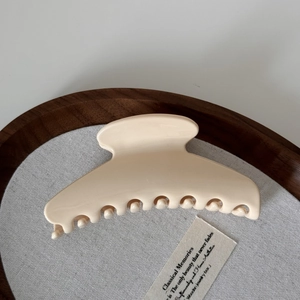 Macro detail of glossy cream-colored large hair claw clip on elegant wooden tray