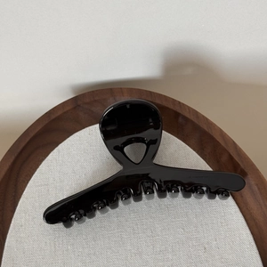 Close-up of a glossy black hair claw clip resting in a wooden tray with fabric lining