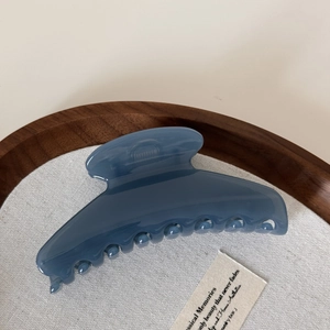 Detail of Morandi blue hair claw clip on wooden tray showcasing glossy finish and sleek curve