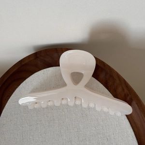 Detailed close-up of glossy cream-white hair claw clip on a rustic wooden tray decor