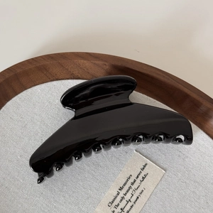 Detail of a large glossy black hair claw clip with a sleek curved handle and rounded teeth
