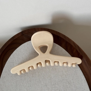Close-up of elegant cream-colored cross claw clip with glossy finish on wooden background