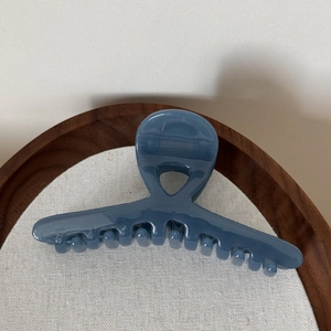 Detail view of a Morandi blue glossy hair claw clip on a textured wooden tray