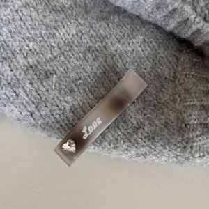 Détail d'une pince à cheveux en acétate gris avec écrit Love et strass en forme de cœur