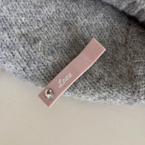 Détail de la barrette rose mate avec texte Love et accent de cœur argenté sur tricot
