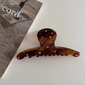 Detailed shot of amber acetate hair claw clip with colorful rhinestones on white table