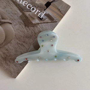 Detail view of light blue acetate hair claw with colorful rhinestones on magazine background
