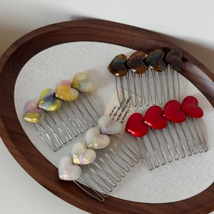Detail of four acetate heart hair combs in tortoiseshell, pearl, red, and gradient colors