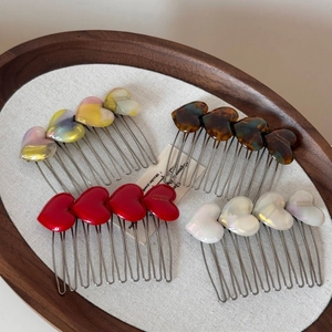 Detailed macro view of acetate heart hair combs in red, tortoiseshell, and pearl finishes