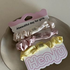 Detaillierte Ansicht von drei Satin-Haargummis in Creme, Rosa und Gelb auf einem Keramikteller