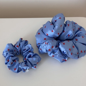 Detail of two light blue satin scrunchies featuring a sweet red heart polka dot pattern