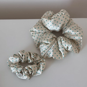 Detailed view of cream satin polka dot scrunchies with elegant silver logo charm