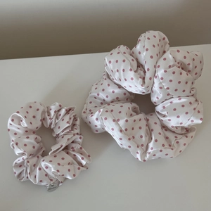 Close-up of pink polka dot satin scrunchies set with a branded metal charm detail