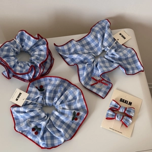 Detail of blue gingham scrunchies and bow clips with red wavy edges and cherry embroidery