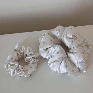 Close-up of white satin scrunchies with blue heart patterns and a small metal logo tag