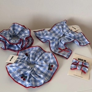 Detail of blue plaid scrunchies with red piping and cherry embroidery on white background