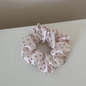 Close-up of a white satin scrunchie with pink polka dots and a metallic logo tag